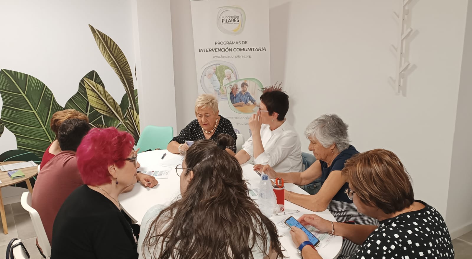 Grupo de personas participando en una reunión de trabajo en una sala, con materiales sobre la mesa, en el marco de los Programas de Intervención Comunitaria de Fundación Pilares